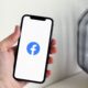 Ruka drži pametni telefon na čijem je zaslonu prikazan logotip Facebooka.