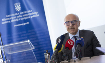 Muškarac u odijelu i naočalama govori pred novinarima, uz više mikrofona i pano Ministarstva rada, mirovinskoga sustava, obitelji i socijalne politike.