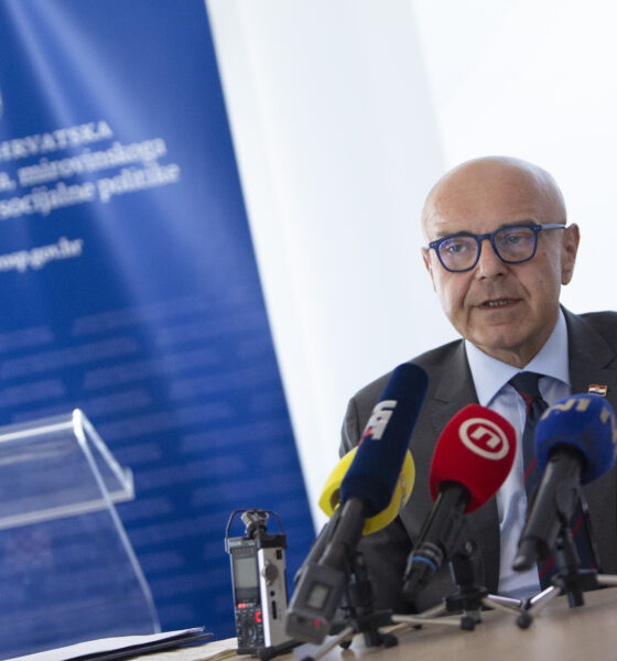 Muškarac u odijelu i naočalama govori pred novinarima, uz više mikrofona i pano Ministarstva rada, mirovinskoga sustava, obitelji i socijalne politike.