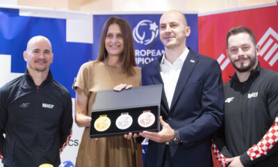 Četvero ljudi pozira na konferenciji za medije držeći kutiju sa zlatnom, srebrnom i brončanom medaljom.