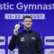 Gimnastičar pozira sa zlatnom medaljom ispred pozadine s natpisom „Artistic Gymnastics“.