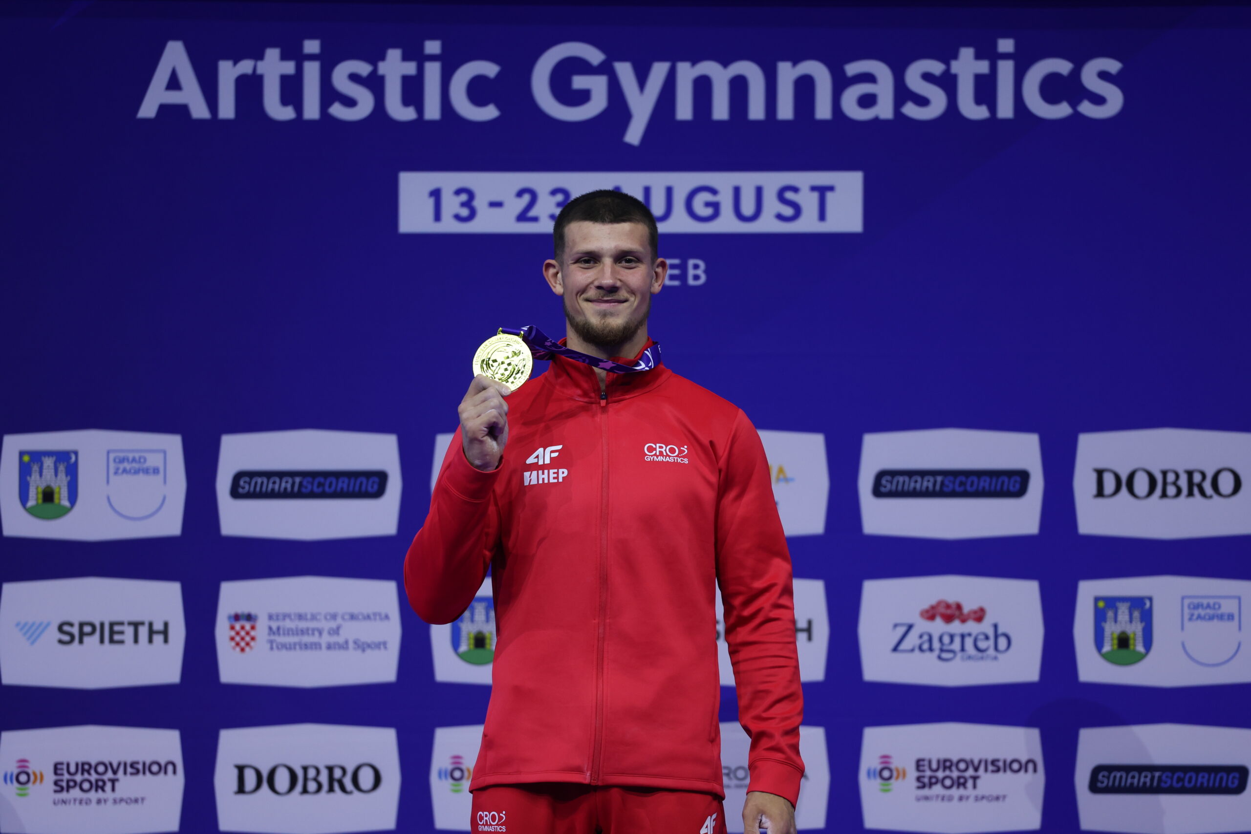 Gimnastičar u hrvatskoj sportskoj opremi pokazuje osvojenu zlatnu medalju.
