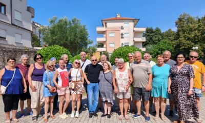 Na fotografiji je veća skupina sudionika edukacijsko-rehabilitacijskog kampa Udruge slijepih USKA, okupljena na otvorenom za zajedničku fotografiju. Sudionici stoje u nekoliko redova, nasmijani i opušteni, a među njima su osobe različite dobi. Odjeveni su u ljetnu odjeću, što odgovara ljetnom boravku u Premanturi. U pozadini se vide stambene zgrade, zelenilo i vedro plavo nebo, dok je cijela skupina obasjana sunčevom svjetlošću. Fotografija dočarava zajedništvo, druženje i dobro raspoloženje sudionika kampa te lijepo prikazuje atmosferu zajedničkog boravka i aktivnosti.