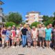 Na fotografiji je veća skupina sudionika edukacijsko-rehabilitacijskog kampa Udruge slijepih USKA, okupljena na otvorenom za zajedničku fotografiju. Sudionici stoje u nekoliko redova, nasmijani i opušteni, a među njima su osobe različite dobi. Odjeveni su u ljetnu odjeću, što odgovara ljetnom boravku u Premanturi. U pozadini se vide stambene zgrade, zelenilo i vedro plavo nebo, dok je cijela skupina obasjana sunčevom svjetlošću. Fotografija dočarava zajedništvo, druženje i dobro raspoloženje sudionika kampa te lijepo prikazuje atmosferu zajedničkog boravka i aktivnosti.