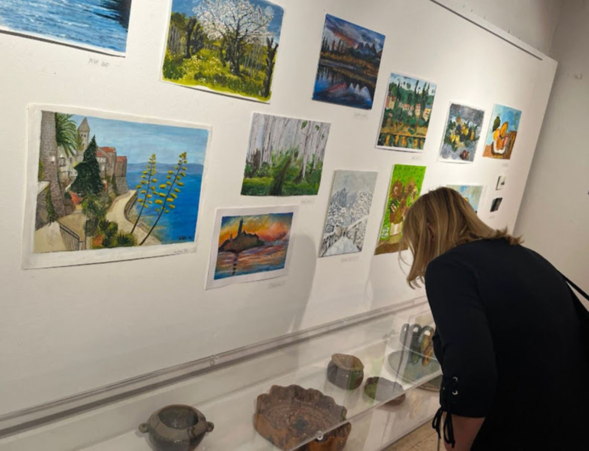 Posjetiteljica razgledava izložene likovne radove i predmete u galerijskom prostoru.
