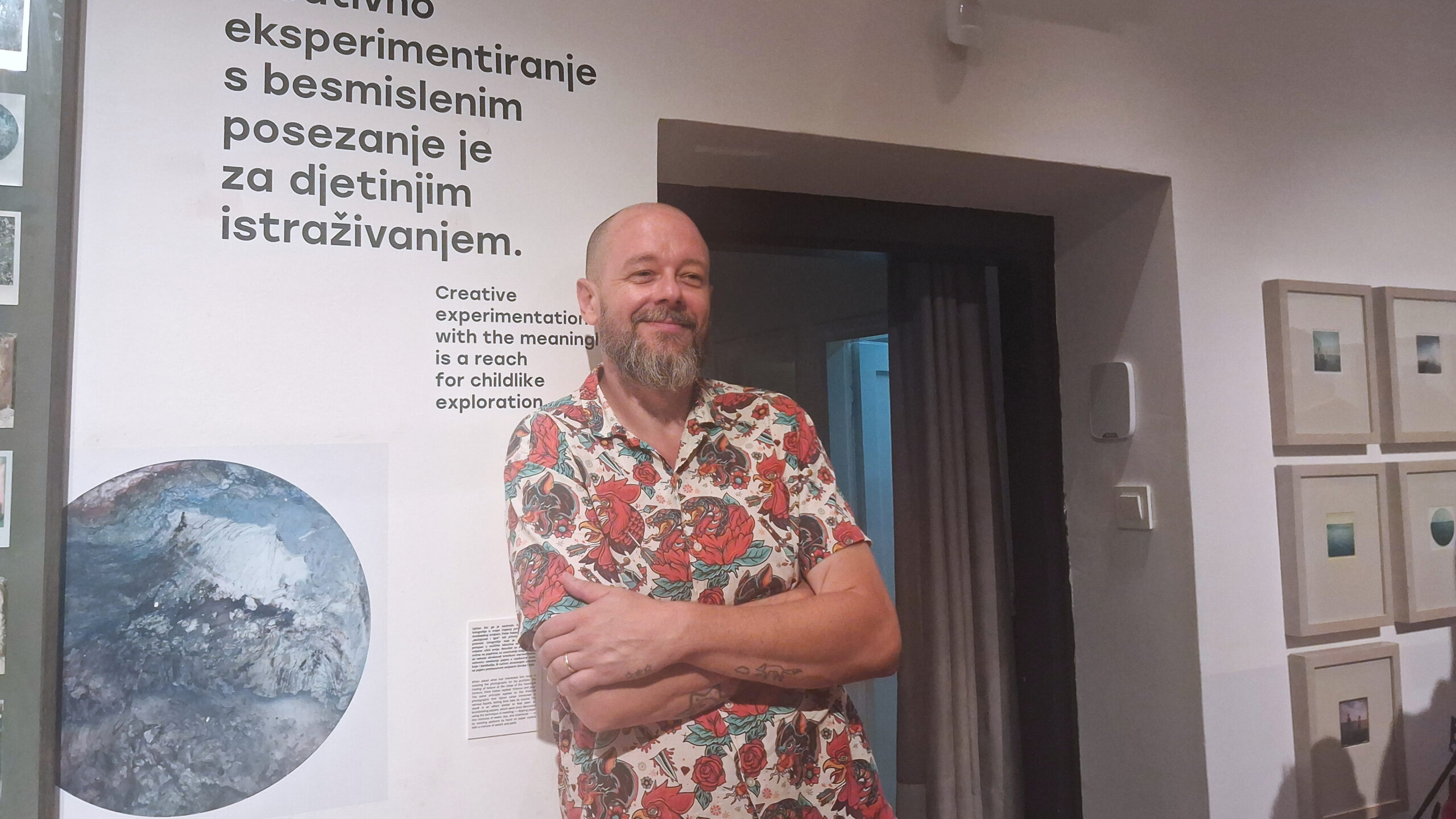Muškarac u šarenoj košulji stoji u galerijskom prostoru okružen umjetničkim radovima.