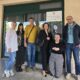 Na fotografiji je šest osoba okupljenih ispred ulaza u zgradu, pozirajući za zajedničku fotografiju. Skupinu čine predstavnici partnerskih organizacija i korisnica projekta, a iza njih na staklenim vratima istaknut je plakat s grbom Republike Hrvatske i informacijom o Programu prekogranične suradnje između Republike Hrvatske i Bosne i Hercegovine. Sudionici stoje nasmiješeni ispred ulaza, dok jedna osoba sjedi u prvom planu. Fotografija je snimljena na otvorenom, pri dnevnom svjetlu, te odaje ozračje suradnje i zajedništva. Istaknuti plakat u pozadini upućuje na provedbu projekta usmjerenog jačanju prekogranične suradnje i unaprjeđenju podrške osobama s invaliditetom i drugim ranjivim skupinama.