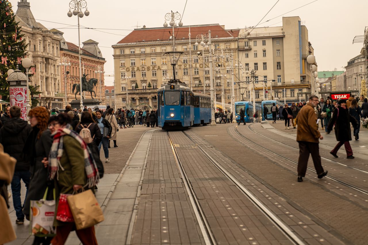 Stari plavi tramvaj prolazi središtem Zagreba među brojnim pješacima.