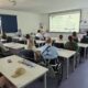 Na fotografiji je prikazana početna konferencija projekta „SRCE ZAJEDNICE“. Sudionici sjede u konferencijskoj dvorani i prate prezentaciju o projektu, dok je jedna osoba ispred projekcijskog platna i predstavlja sadržaj. U prvom planu i među sudionicima vidljive su osobe u invalidskim kolicima, čime fotografija dodatno naglašava uključivost i usmjerenost projekta na osobe s invaliditetom. U pozadini se nalaze promotivni materijali i roll-up plakati projekta „SRCE ZAJEDNICE“.