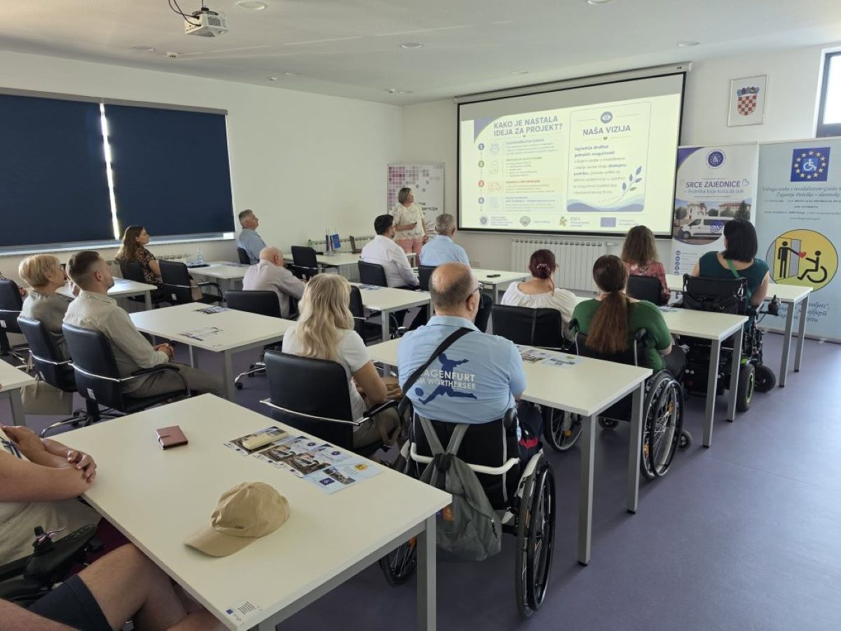 Na fotografiji je prikazana početna konferencija projekta „SRCE ZAJEDNICE“. Sudionici sjede u konferencijskoj dvorani i prate prezentaciju o projektu, dok je jedna osoba ispred projekcijskog platna i predstavlja sadržaj. U prvom planu i među sudionicima vidljive su osobe u invalidskim kolicima, čime fotografija dodatno naglašava uključivost i usmjerenost projekta na osobe s invaliditetom. U pozadini se nalaze promotivni materijali i roll-up plakati projekta „SRCE ZAJEDNICE“.