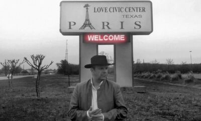 Crno-bijela fotografija muškarca s kaubojskim šeširom ispred znaka ‘Paris’ i ‘Love Civic Center’ u Teksasu.