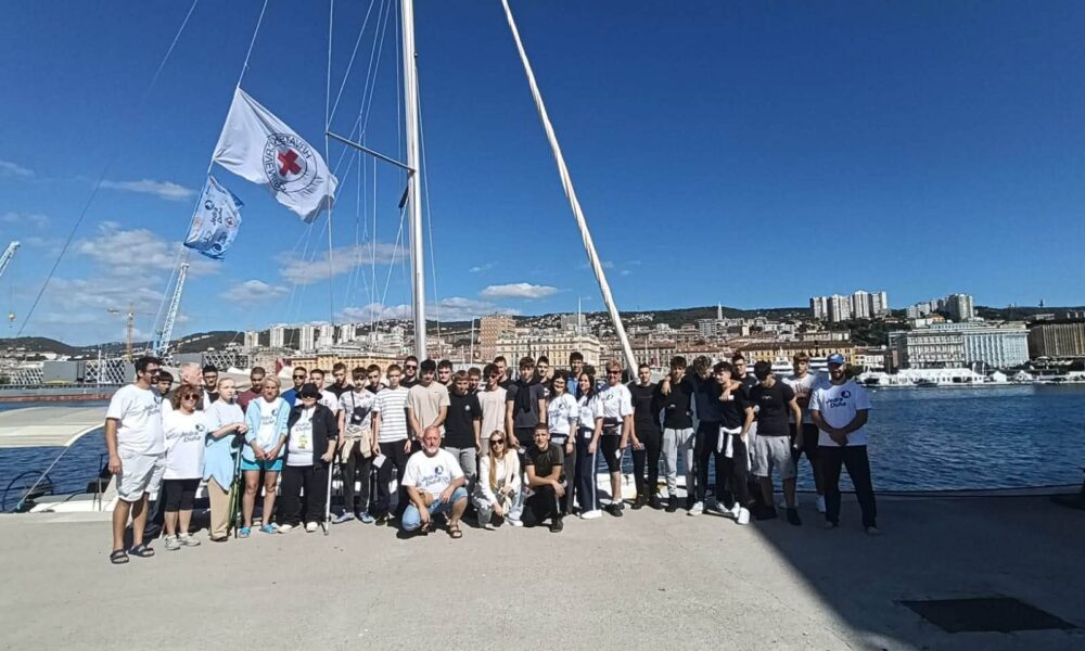 Na fotografiji je velika skupina sudionika projekta „Jedra duha“ okupljena na riječkoj rivi, ispred jedrilice. U prvom planu stoje i sjede sudionici različitih generacija, a među njima su i mladi sudionici te članovi organizacijskog i partnerskog tima. U pozadini se vidi riječki zaljev s gradskom obalom i prepoznatljivom panoramom Rijeke. Na jedrilici se vijore zastave Hrvatskog Crvenog križa i projekta, dok vedro nebo i sunčano vrijeme stvaraju vedru atmosferu. Fotografija dobro prikazuje zajedništvo, inkluziju i druženje sudionika projekta „Jedra duha“, kao i povezanost projekta s morem i jedrenjem.
