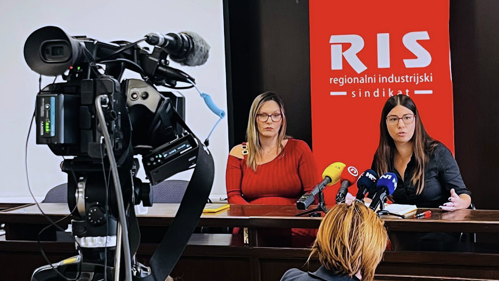 Dvije žene govore na konferenciji za medije Regionalnog industrijskog sindikata, ispred novinarskih mikrofona.