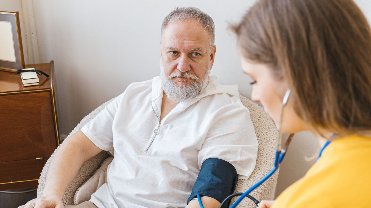 Stariji muškarac sjedi na stolcu dok mu zdravstvena djelatnica obavlja preventivni pregled.