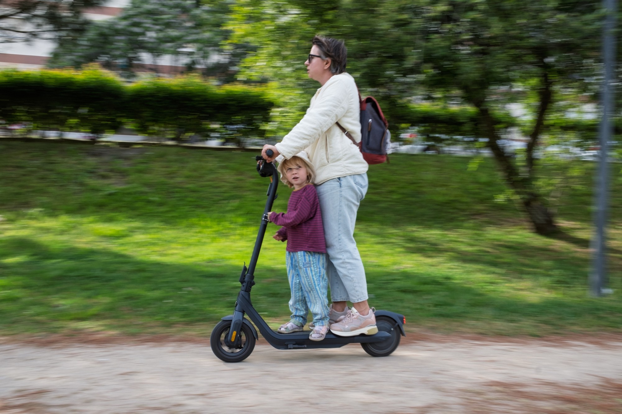 Odrasla osoba i dijete zajedno se voze na električnom romobilu kroz park.