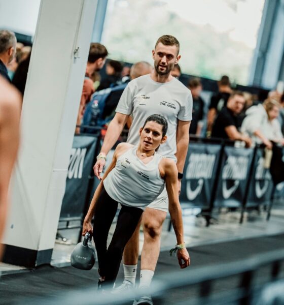 Sportašica s girjom u ruci tijekom natjecanja, uz trenera koji stoji iza nje.