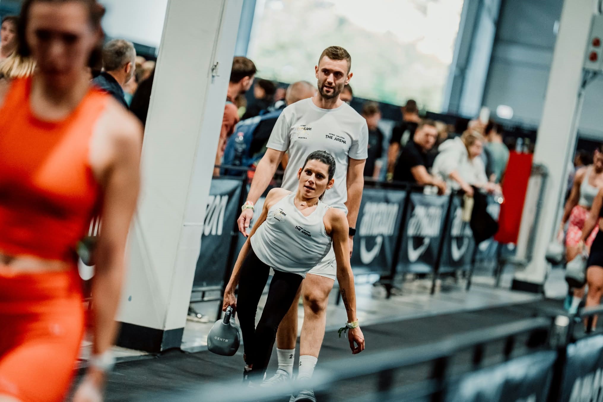 Sportašica s girjom u ruci tijekom natjecanja, uz trenera koji stoji iza nje.