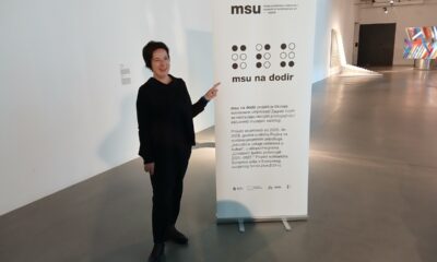 Žena u crnoj odjeći pokazuje na informativni pano projekta „MSU na dodir“ u Muzeju suvremene umjetnosti u Zagrebu.