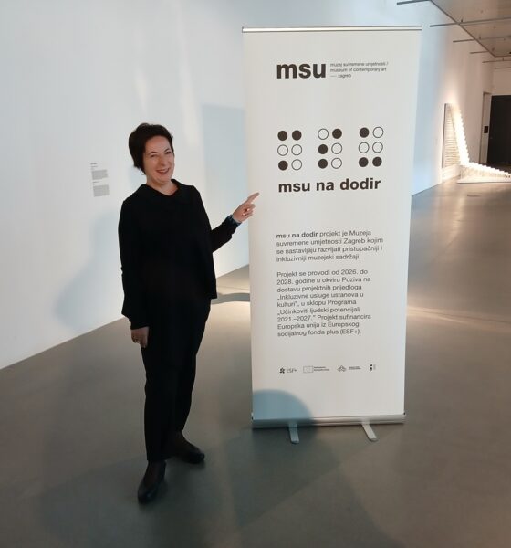 Žena u crnoj odjeći pokazuje na informativni pano projekta „MSU na dodir“ u Muzeju suvremene umjetnosti u Zagrebu.