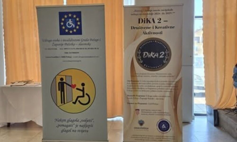 Na fotografiji se nalaze dva promotivna roll-up plakata Udruge osoba s invaliditetom Grada Požege i Požeško-slavonske županije. Na desnom plakatu predstavljen je program „DiKA 2 – Društvene i kreativne aktivnosti“, dok se na lijevom nalazi simbol pristupačnosti i ilustracija koja prikazuje pružanje pomoći osobi u invalidskim kolicima. Plakati su postavljeni u zatvorenom prostoru, uz prozore prekrivene žutim zavjesama. Fotografija prikazuje promotivne materijale kojima se predstavljaju rad Udruge, program DiKA 2 i važnost podrške osobama s invaliditetom.