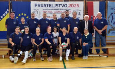 Fotografija prikazuje nekoliko ljudi u tamnoplavim dresovima, dio ih sjedi, dok drugi dio stoji. Čovjek u odjelu nosi štaku, a tu je još nekoliko štaka na podu. Na fotografiji je i hrvatska zastava te plakat na kojem piše "Prijateljstvo 2025".