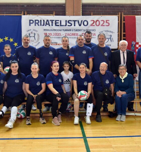Fotografija prikazuje nekoliko ljudi u tamnoplavim dresovima, dio ih sjedi, dok drugi dio stoji. Čovjek u odjelu nosi štaku, a tu je još nekoliko štaka na podu. Na fotografiji je i hrvatska zastava te plakat na kojem piše "Prijateljstvo 2025".