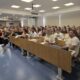Na fotografiji je prikazana radionica ili predavanje u fakultetskoj učionici. U prostranoj i moderno opremljenoj dvorani nalazi se veći broj studenata i drugih sudionika koji prate izlaganje. U prednjem dijelu prostorije vidi se predavač koji se obraća publici, dok je uz njega osoba koja sudjeluje u izlaganju. Učionica je opremljena projektorom, računalom i velikim ekranom. Sudionici sjede u nekoliko redova i pažljivo prate predavanje, a neki vode bilješke. Fotografija dobro prikazuje aktivno sudjelovanje i zainteresiranost sudionika te atmosferu akademskog okupljanja i edukacije.