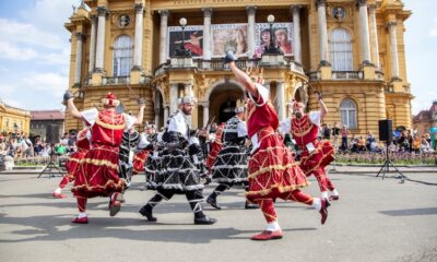 Folklorni plesači u raskošnim crvenim i crnim kostimima nastupaju ispred Hrvatskog narodnog kazališta u Zagrebu.