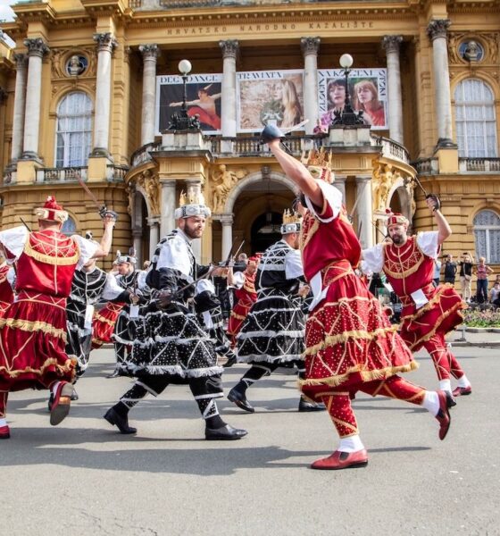 Folklorni plesači u raskošnim crvenim i crnim kostimima nastupaju ispred Hrvatskog narodnog kazališta u Zagrebu.