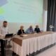 Sudionici radionice za zaposlenike udruga osoba s invaliditetom sjede za stolom, dok muškarac stoji za govornicom.