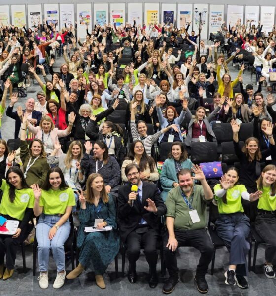 Na fotografiji je velika skupina sudionika ATAAC konferencije, okupljena u konferencijskoj dvorani. Gotovo svi sudionici veselo poziraju prema kameri s podignutim rukama, stvarajući vrlo energičnu i pozitivnu atmosferu. U prvom planu su organizatori i članovi volonterskog tima u prepoznatljivim zelenim majicama, dok se u pozadini vide brojni sudionici, izlagački panoi i prostor konferencije. Fotografija dobro dočarava zajedništvo, velik odaziv i opuštenu atmosferu ATAAC-a.